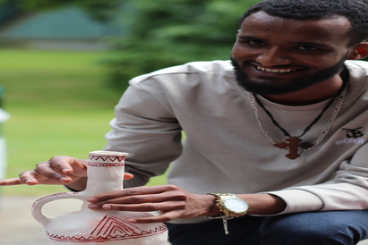 Grmalem Kasa, Eritrean clay artist, posing with a clay coffee pot made previously, at the Cambridge Refugee Week Community Arts Festival, on 22 June 2024.