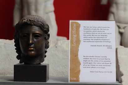 A Classical Greek bronze head, possibly of Apollo, on display at the Museum of Classical Archaeology at Cambridge University. On its right is a display comparing the voyage of Ulysses as described by Ovid to the modern-day journeys of refugees.