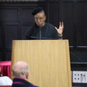 Professor Tendayi Achiume giving a lecture at a podium, in the lecture hall of The Divinity School, St John's College. She is standing in front of a wood panelled wall, facing outwards towards her audience. 